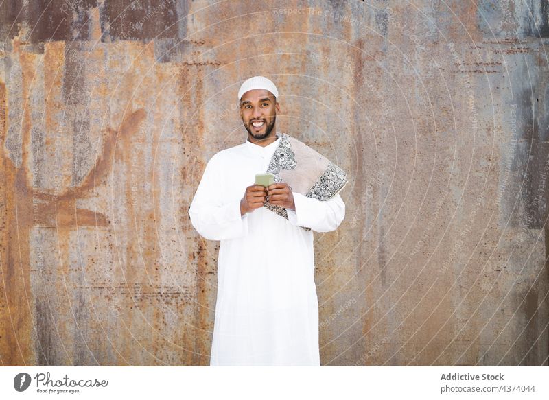 Islamischer Mann benutzt Smartphone auf der Straße muslimisch arabisch benutzend Lächeln Tradition Wand schäbig soziale Netzwerke ruhen männlich Funktelefon