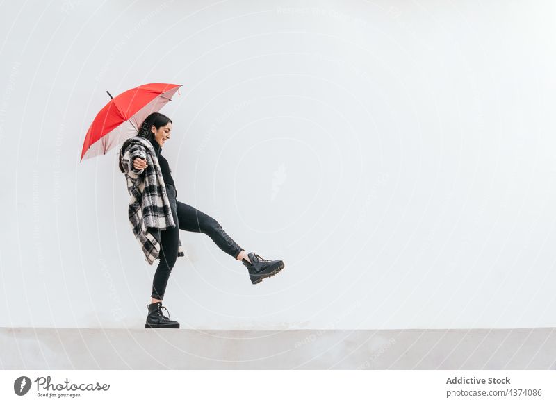 Junge Frau mit Regenschirm balanciert auf Grenze Gleichgewicht Spaziergang Borte Straße Glück Wetter urban Großstadt jung Herbst heiter lässig Lächeln Gebäude