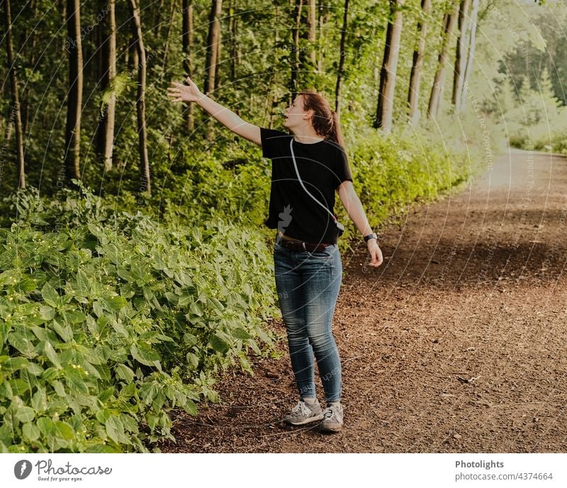 Junge Frau auf einem Waldweg wirft einen grünen Zweig in die Büsche wegwerfen zeigen deuten braun Natur Umwelt Baum Pflanze Außenaufnahme Farbfoto natürlich Tag