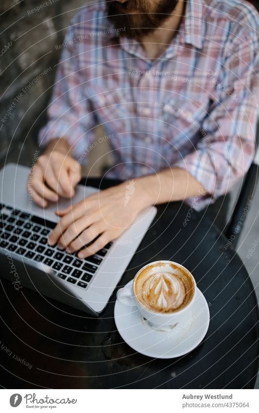 Junger Mann arbeitet an seinem Laptop in einem Café im Freien 25-30 30-35 Jahre Erwachsener Amerikaner Vollbart bärtig Blogger Chef brünett Geschäftsinhaber