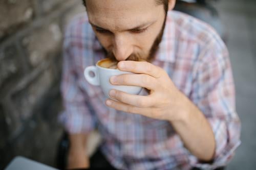 Junger Mann trinkt Kaffee in einem Café im Freien 25-30 30-35 Jahre Erwachsener Amerikaner Vollbart bärtig Blogger Chef brünett Geschäftsinhaber Kalifornien