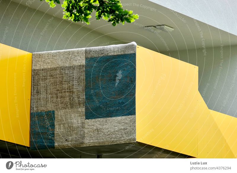 Alltagsgrafik: ein Teppich aufgehängt vor gelber Außenwand, darüber etwas grünes Laub Grafische Darstellung Quadrate Rechtecke graphisch Linie abstrakt