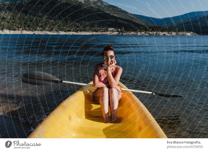 lächelnde kaukasische Frau in Badekleidung hält Ruder sitzen auf gelben Kanu in See während sonnigen Tag. Sommerzeit. Sport, Abenteuer und Natur Rudern Glück