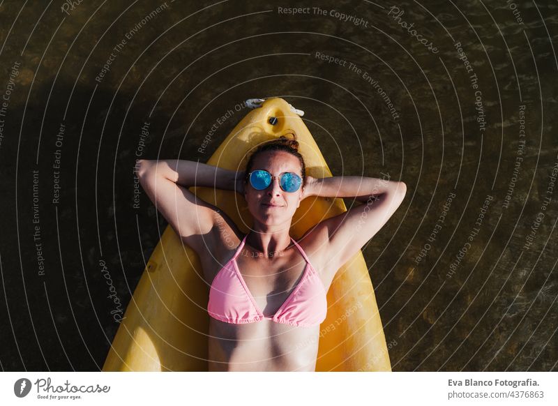 Draufsicht auf glückliche kaukasische Frau auf gelben Kanu im See während des sonnigen Tages liegend. Sommerzeit. Sport, Abenteuer und Natur. Frau in Badehose und Sonnenbrille