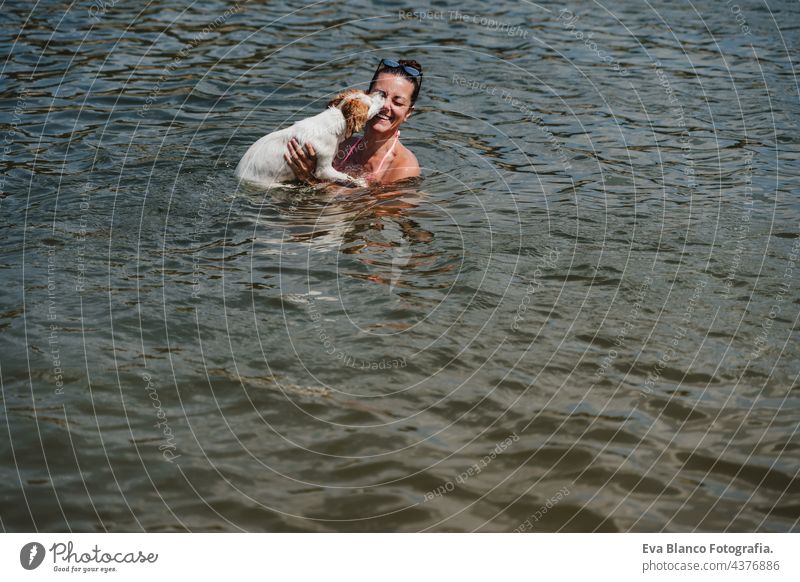 kaukasische Frau und niedlichen Jack Russell Hund schwimmen im See und Spaß haben zusammen. Hund lecken Besitzer. Urlaub und entspannen Konzept jack russell