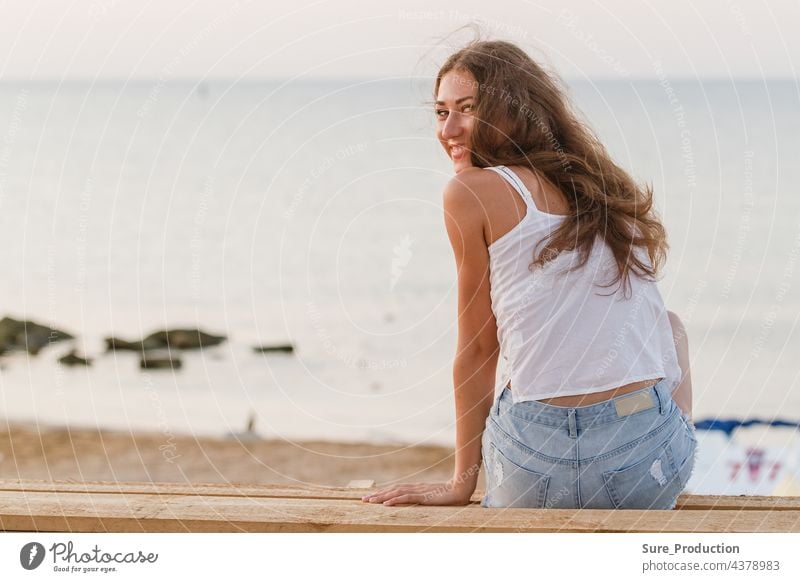 bezaubernde junge Frau am Strand in den Strahlen der aufgehenden Sonne sexy Mädchen lockig brünett schlank weiß Porträt hübsch Dame fliegen Behaarung steigend