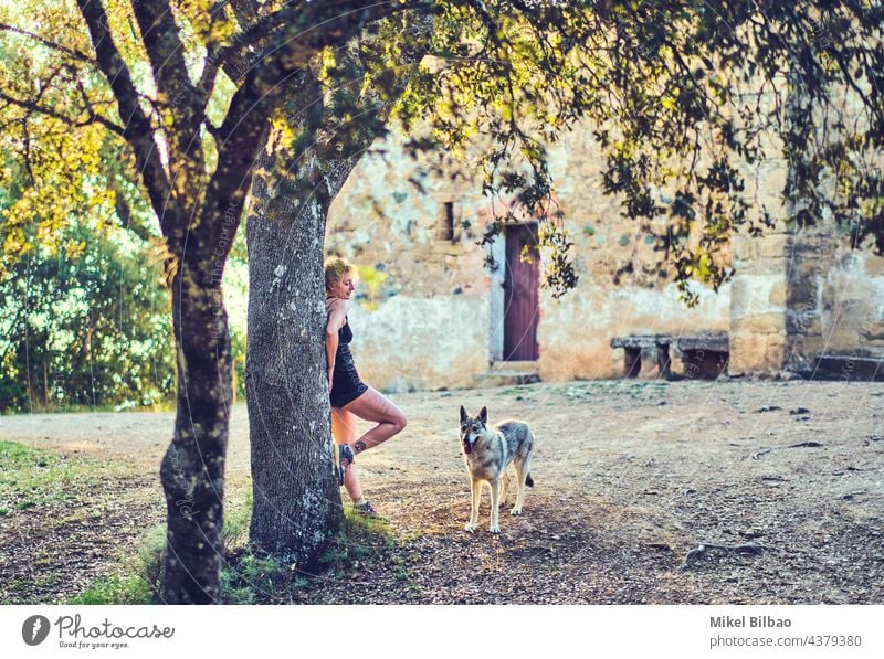 Reife kaukasische Frau im Freien stehend mit einem Wolfshund in einer ländlichen Gegend mit Bäumen und einem Haus. Lebensstile Menschen reif jung Frauen