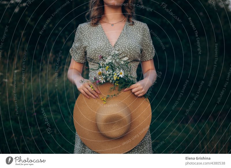 Ein junges Mädchen hält einen Hut und einen Strauß Wildblumen in den Händen. Kleid Sommer Blumenstrauß Sommerabend Sonne Margeriten Feld Romantik Weiblichkeit