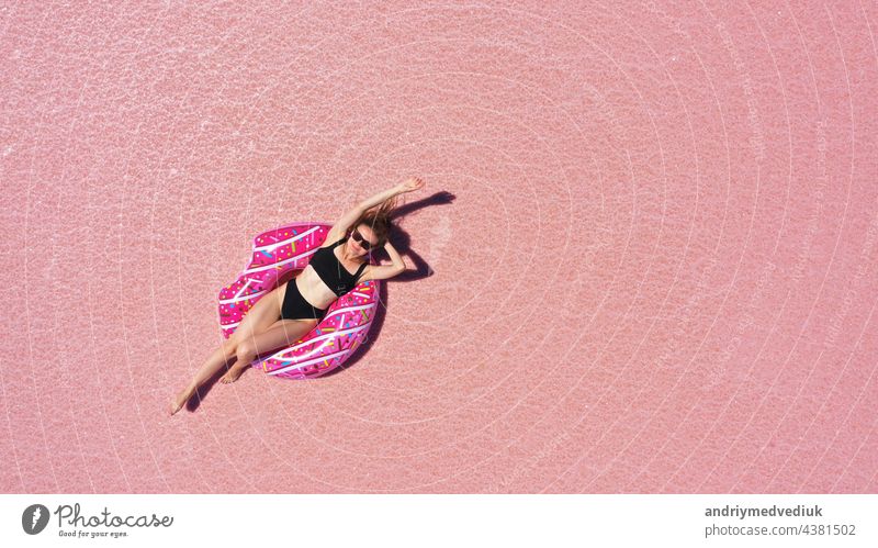 Luftaufnahme von Beautiful woman lying in a bikini on inflatable mattress on pink salt lake. copy space. opening of the tourist season. summer holiday concept. taken from above from a drone