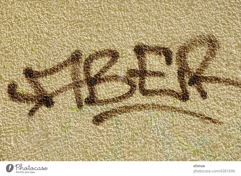 ABER steht in braunen Großbuchstaben an der beigefarbenen, grob verputzten Wand / Einwand aber Graffito Graffiti Farbe Wort Gebäude Subkultur Schmiererei