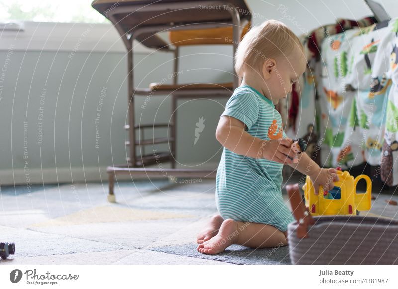 14 Monate altes Baby spielt mit einem Schulbus-Spielzeug und Figuren; Kinderzimmer und Vintage-Schreibtisch im Hintergrund eigenständiges Spiel einsetzen