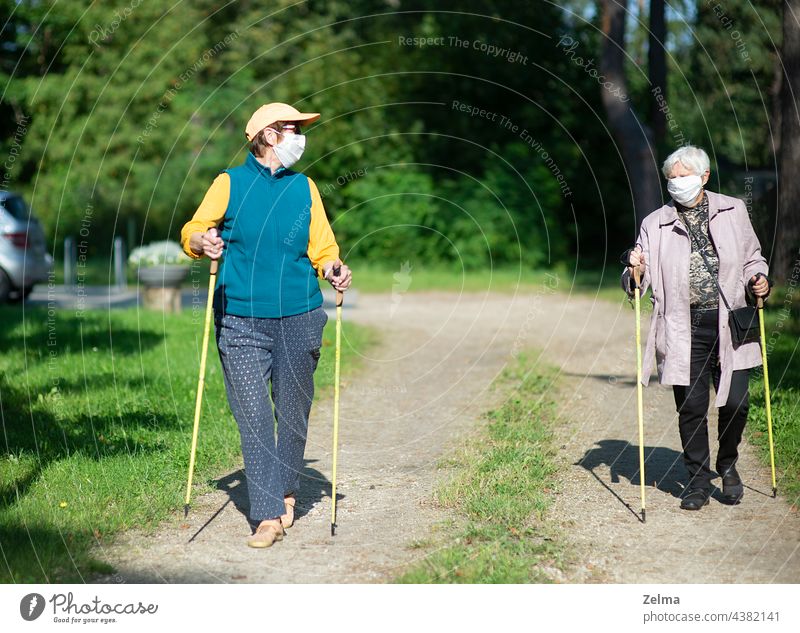 Zwei ältere Frauen mit medizinischen Masken gehen mit Nordic-Walking-Stöcken während der Covid-19-Pandemie Nordic Walking Lifestyle Freizeit Senior Menschen