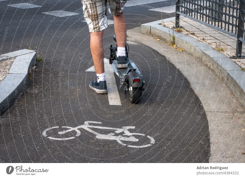 Detail eines Elektrorollers, der von einem Mann gefahren wird, während er wartet, bis er an der Reihe ist, eine Straße zu überqueren. E-Scooter ist auf Fahrradspuren erlaubt.