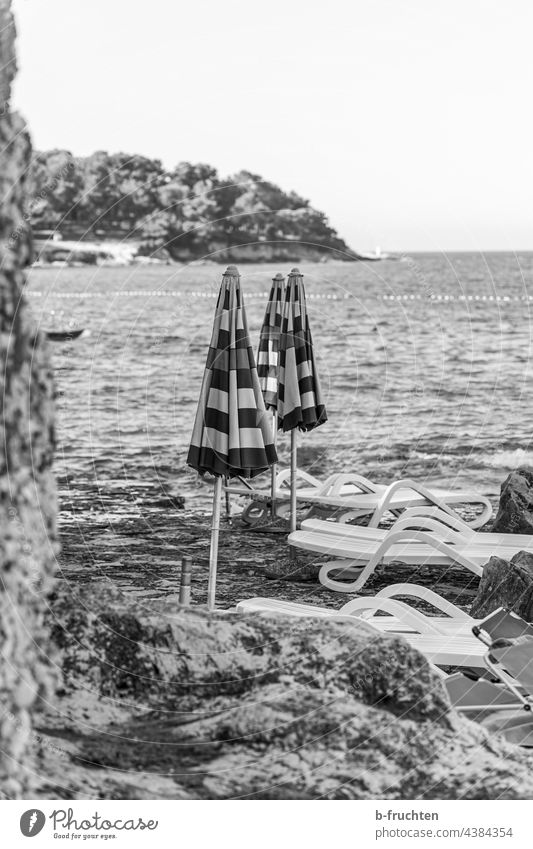 geschlossene Sonnenschirme am Strand Meer Sonnenliege Felsen Kroatien Wasser Schwarzweißfoto morgen Bucht allein Einsamkeit