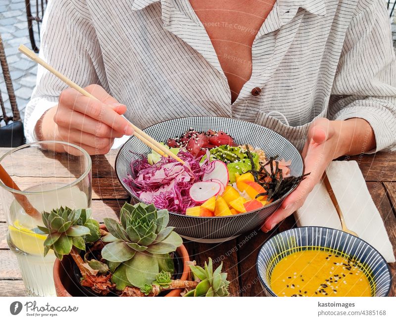Frau essen leckere bunte gesunde natürliche organische vegetarische Hawaiian poke Schüssel mit asiatischen Stäbchen auf rustikalen Holztisch. Gesunde natürliche organische Essen Konzept