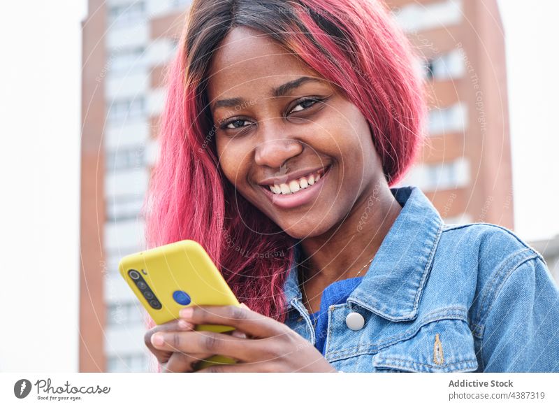 Flippige ethnische Frau mit Smartphone auf der Straße Nachricht Stil gefärbtes Haar Farbe urban informell Hipster jung schwarz Afroamerikaner tausendjährig