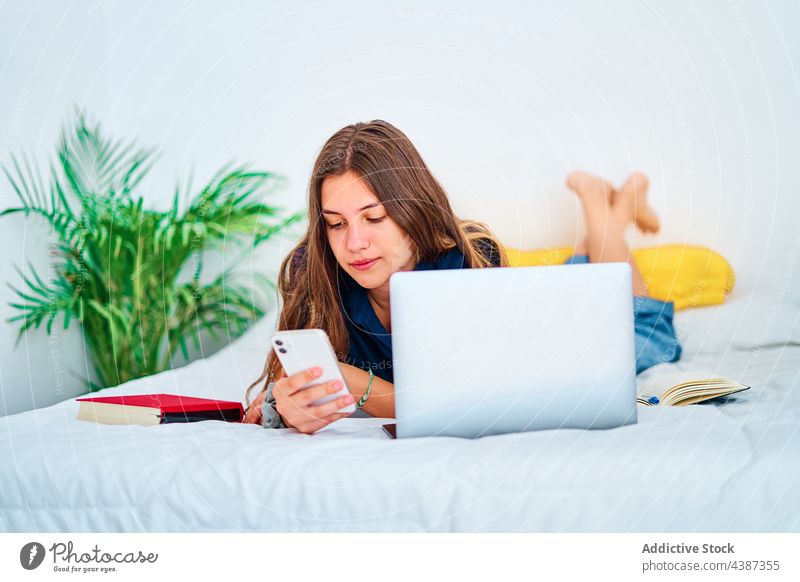 Teenager mit Gadgets beim Online-Studium zu Hause Frau Schüler online Apparatur benutzend Bett lernen abgelegen Bildung jung Laptop Smartphone Internet Gerät
