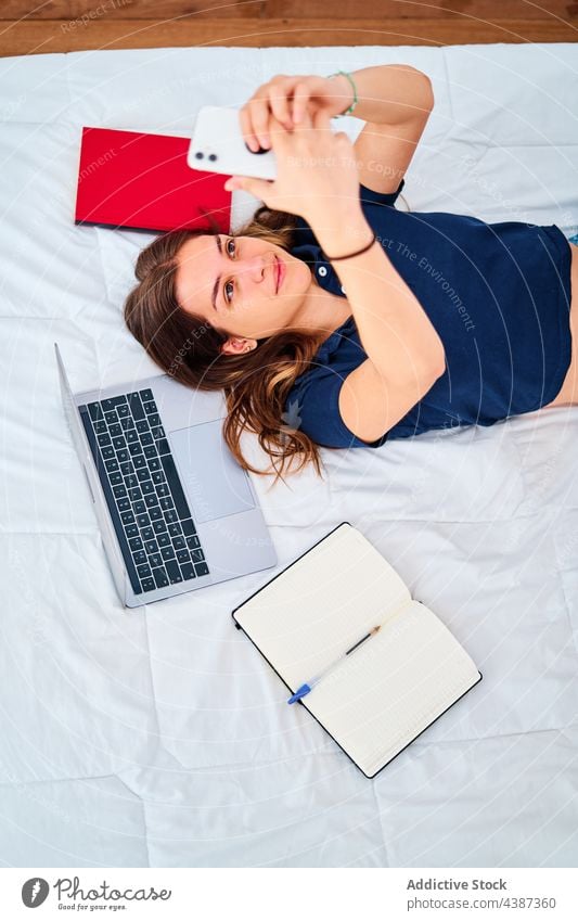 Teenager mit Gadgets beim Online-Studium zu Hause Frau Schüler online Apparatur benutzend Bett Selfie lernen abgelegen Bildung jung Laptop Smartphone Lächeln