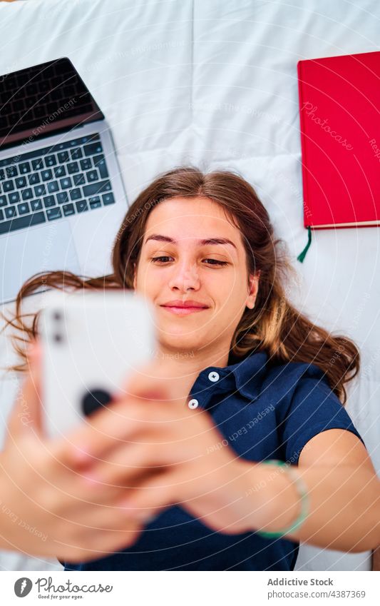 Studentin macht Selfie mit Smartphone Frau Schüler zu Hause online Apparatur Bett Pause abgelegen jung fotografieren Gerät Laptop Mobile benutzend Internet