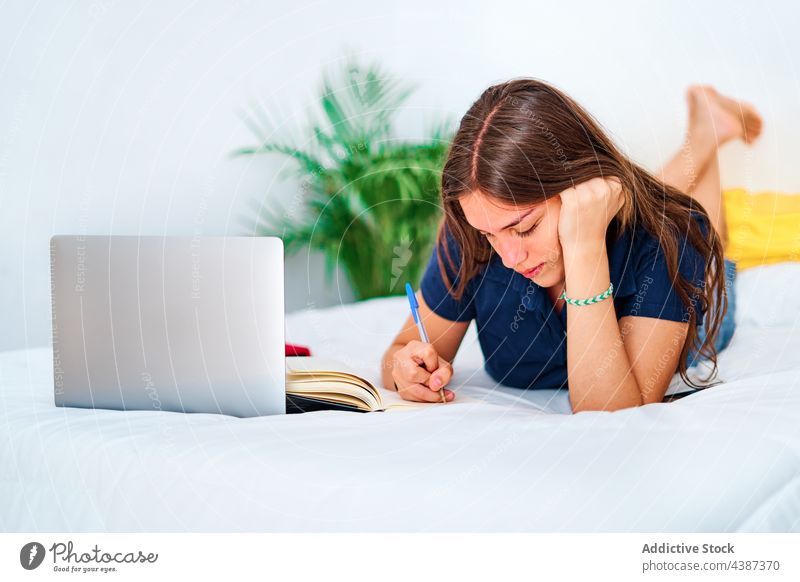 Junge Frau studiert online im Schlafzimmer Schüler schreiben Laptop Bett lernen zu Hause abgelegen Bildung Apparatur jung Teenager zur Kenntnis nehmen Internet