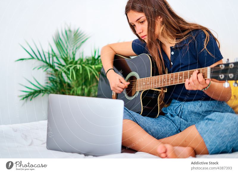Junge Frau mit Laptop spielt Gitarre spielen Musik lernen online zu Hause akustisch üben Schüler jung Hobby Lektion Tutorial Instrument zuschauen Bildung