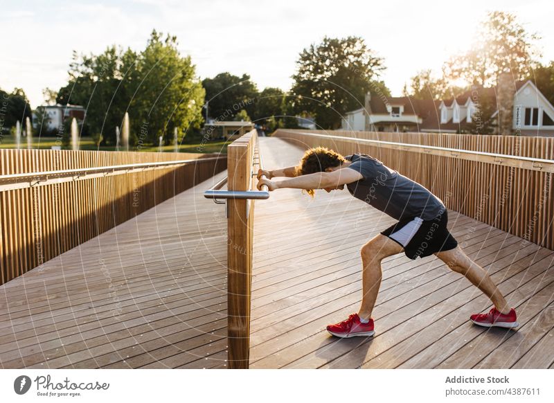 Sportler beim Aufwärmen der Beine während des Trainings auf der Holzpromenade Athlet Promenade Spazierweg Dehnung Übung beweglich männlich Mann Sommer Vitalität