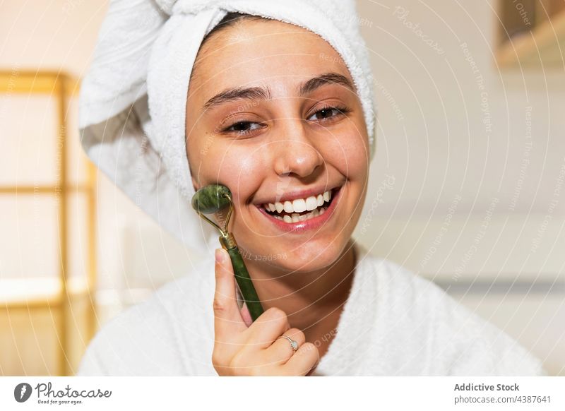 Junge Frau massiert Gesicht mit Jadewalze Massage Rolle Hautpflege Lächeln heimwärts Routine Glück Sauberkeit Leckerbissen Schönheit Spa täglich Verfahren