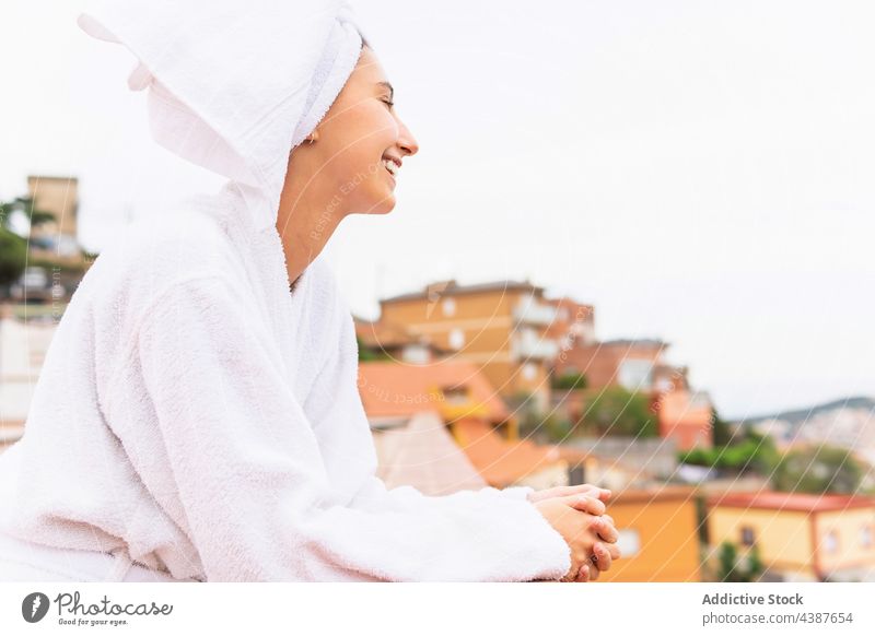 Fröhliche Frau ruht sich nach dem Duschen auf dem Balkon aus ruhen Hautpflege Routine Wochenende Hygiene Lächeln Morgen jung heiter Verfahren Spa Handtuch