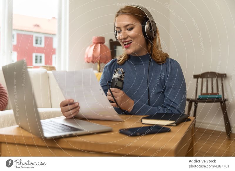 Gut gelaunte Frau, die einen Podcast aufnimmt und ein Mikrofon benutzt Aufzeichnen sprechen reden Kopfhörer Wirt Radio lesen Hinweis Papier Ausstrahlung Lächeln