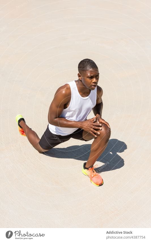 Schwarzer Sportler streckt die Beine beim Training im Sommer schwarz Dehnung Mann Aufwärmen Ausfallschritt Übung Athlet beweglich männlich Afroamerikaner