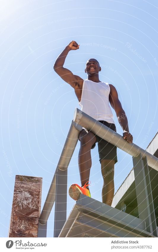 Glücklicher schwarzer Sportler feiert seinen Erfolg auf einer Terrasse in der Stadt feiern Sieg Triumph genießen Tor erreichen Gewinner Athlet männlich ethnisch