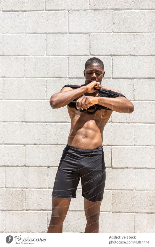 Muskulöser schwarzer Sportler beim Anziehen eines Tanktops auf der Straße angezogen passen Torso stark muskulös Athlet Sportbekleidung Großstadt männlich