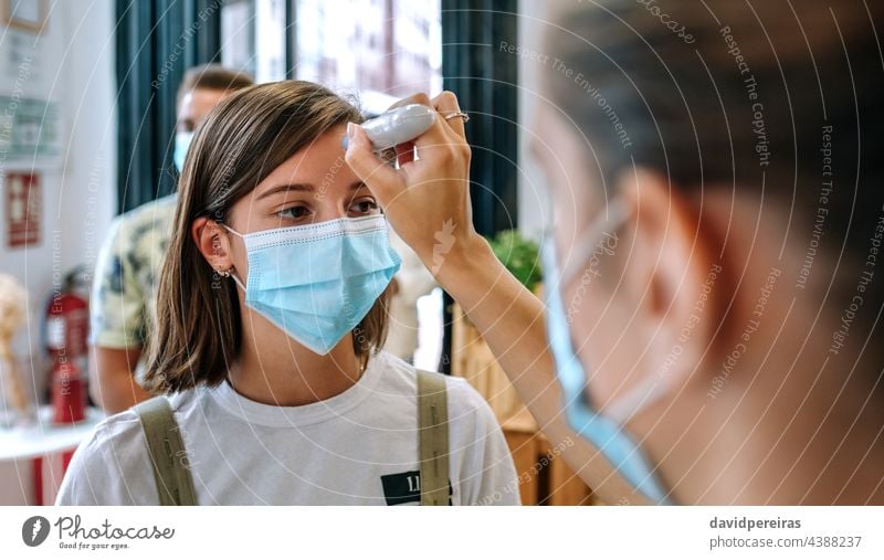 Geschäftsinhaber überprüft Kunden auf Fieber Frau Überprüfung Temperatur berührungsloses Thermometer Coronavirus covid-19 Mitarbeiter Arbeitnehmer Gesichtsmaske