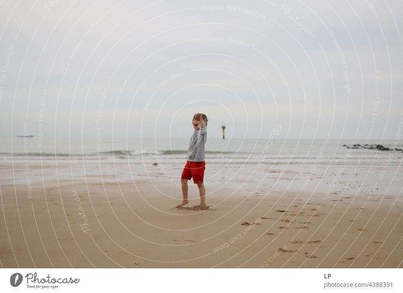 Kind allein am Strand, das einen Arm in Richtung der Kamera zeigt positive Emotion Lächeln Meer Risiko Sehnsucht einzeln vereinzelt Single abstrakt Bewegung