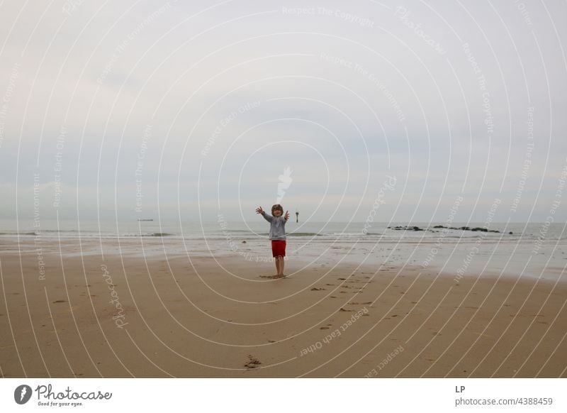 Kind allein am Strand mit offenen Armen in Richtung der Kamera positive Emotion Lächeln Meer Risiko Sehnsucht einzeln vereinzelt Single abstrakt Bewegung