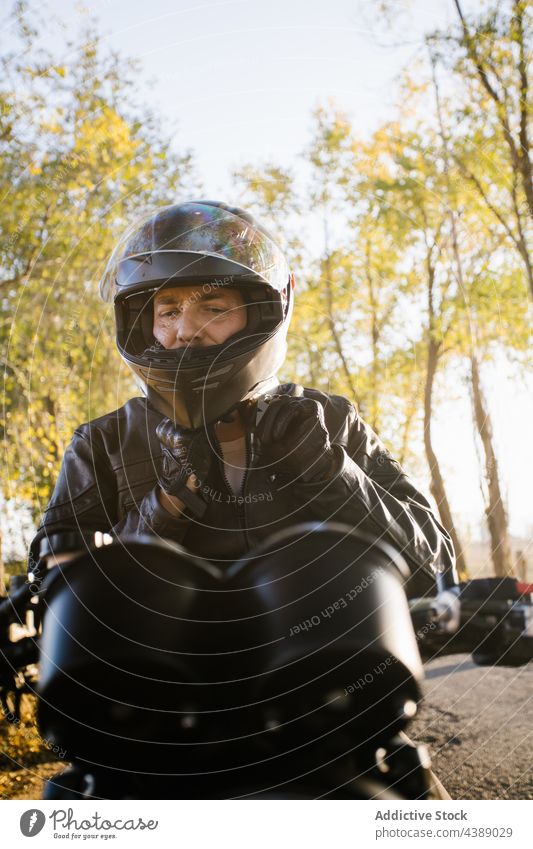 Fokussierter reifer männlicher Biker, der sich auf das Fahren im sonnigen Tag vorbereitet Schutzhelm Motorrad Mann Reiter Aktion aktiv Abenteuer Herbst