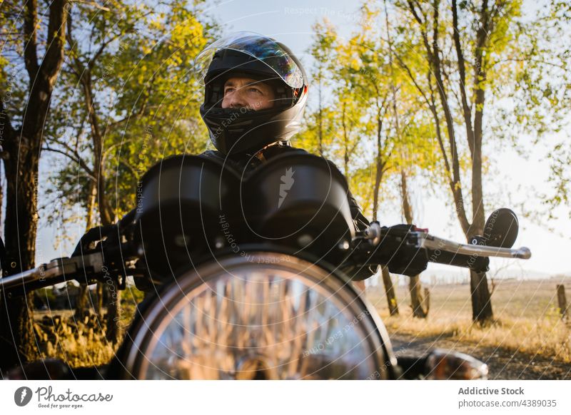 Fokussierter reifer männlicher Biker, der sich auf das Fahren im sonnigen Tag vorbereitet Motorrad Schutzhelm Mann Abenteuer Reiter reisen Straße Aktion aktiv