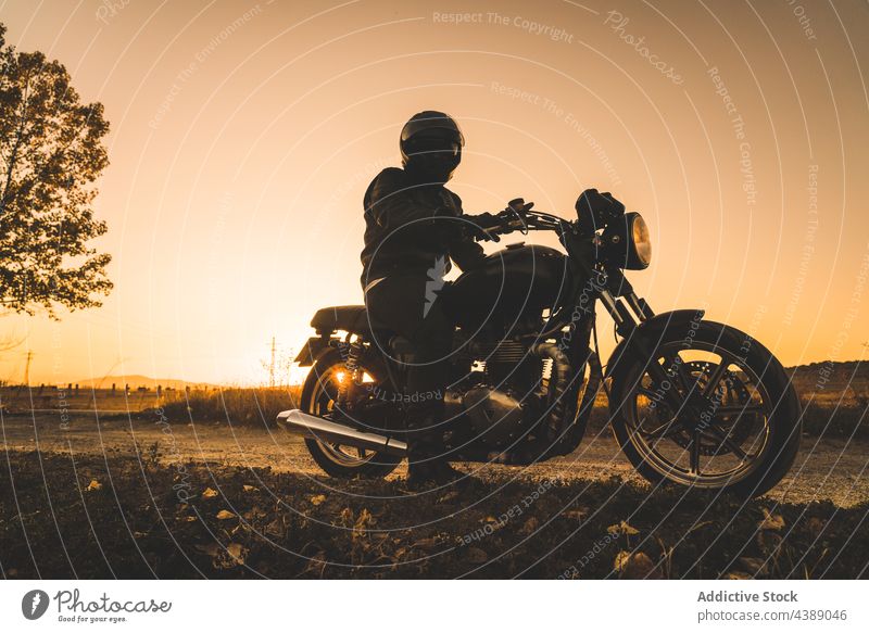Unbekannter Rennfahrer fährt Motorrad bei Sonnenuntergang in ländlicher Umgebung Biker Schatten Schutzhelm Straße reisen aktiv Adrenalin Abenteuer anonym