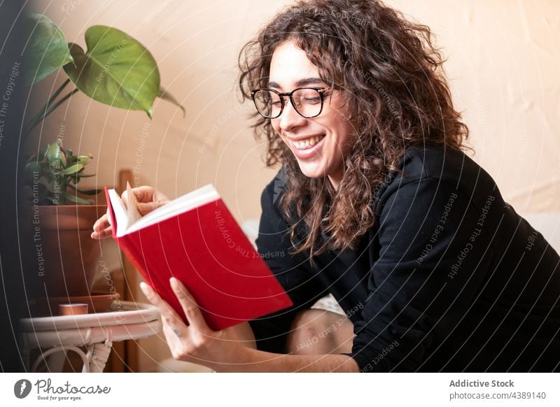 Junge lächelnde Frau mit Brille liest ein Buch lesen Hobby Etage Freizeit Literatur lernen Wissen jung krause Haare hispanisch ethnisch Spektakel Roman ruhen
