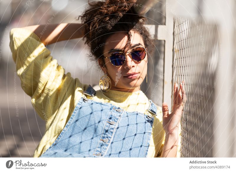 Stilvolle junge Frau mit Sonnenbrille trendy Mode Accessoire modern urban Sonnenlicht tausendjährig Brille Jeansstoff gelb krause Haare hispanisch ethnisch