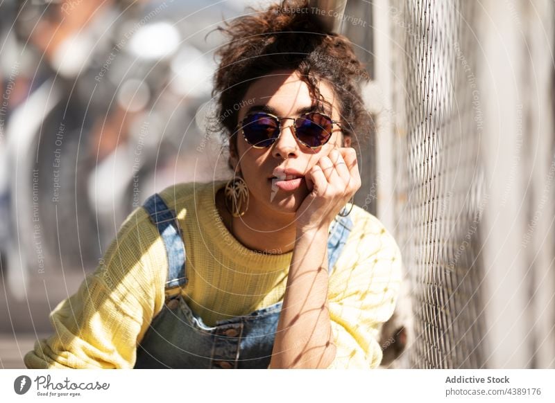 Stilvolle junge Frau mit Sonnenbrille trendy Mode Accessoire modern urban Sonnenlicht tausendjährig fettarm Hand Brille Jeansstoff gelb krause Haare hispanisch