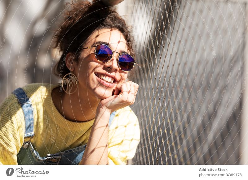 Stilvolle glückliche junge Frau mit Sonnenbrille trendy Mode Accessoire modern urban Sonnenlicht tausendjährig Brille Jeansstoff gelb krause Haare hispanisch