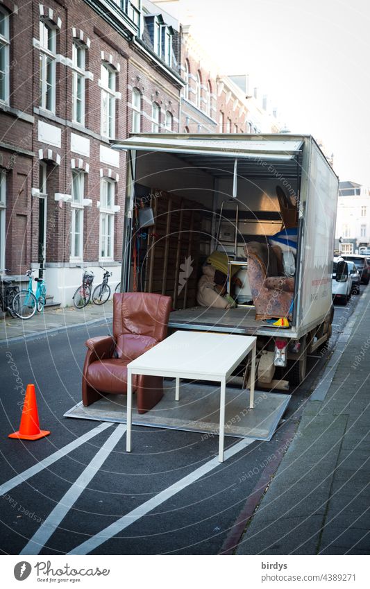 Umzug mit einem Möbelwagen in der Stadt. Möbeltransport. Mietpreise Umzug (Wohnungswechsel) möbeltransport Straße umziehen Tisch Sessel LKW Hebebühne