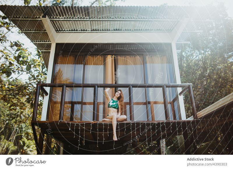 Frau im Bikini sitzt auf dem Balkon eines Strandhauses Badebekleidung Haus Sommer reisen Urlaub sich[Akk] entspannen Tourismus Stil jung Strandbekleidung sitzen
