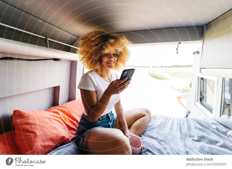 Afroamerikanischer Reisender benutzt Mobiltelefon im Wohnmobil Frau Smartphone benutzend Anhänger Bett ruhen Sommer Wochenende Autoreise Browsen positiv Telefon