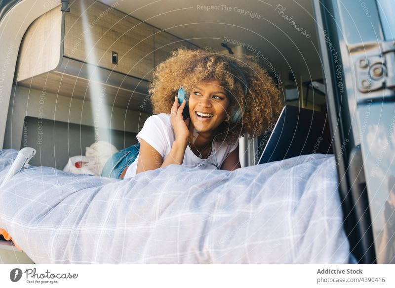 Schwarze Frau benutzt Netbook und hört Musik im Wohnwagen Laptop benutzend Bett Tourismus entfernt Lächeln zuhören soziale Netzwerke Autoreise Glück ruhen jung