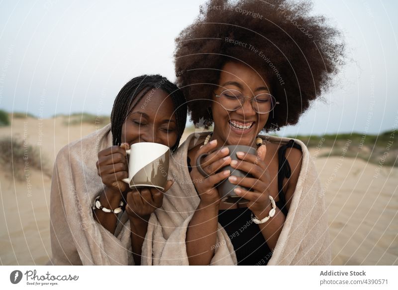 Fröhliche schwarze Freundinnen trinken Kaffee am Strand warm heiter Sommer Frauen Glück Zusammensein Tasse bester Freund Urlaub Feiertag jung Afroamerikaner