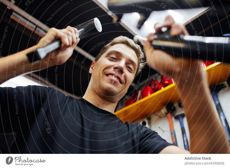 Lächelnder Mann repariert Fahrrad in einer Werkstatt Mechaniker fixieren Reparatur Hammer Dienst Garage männlich Werkzeug heiter Freude Inhalt Arbeit Gerät