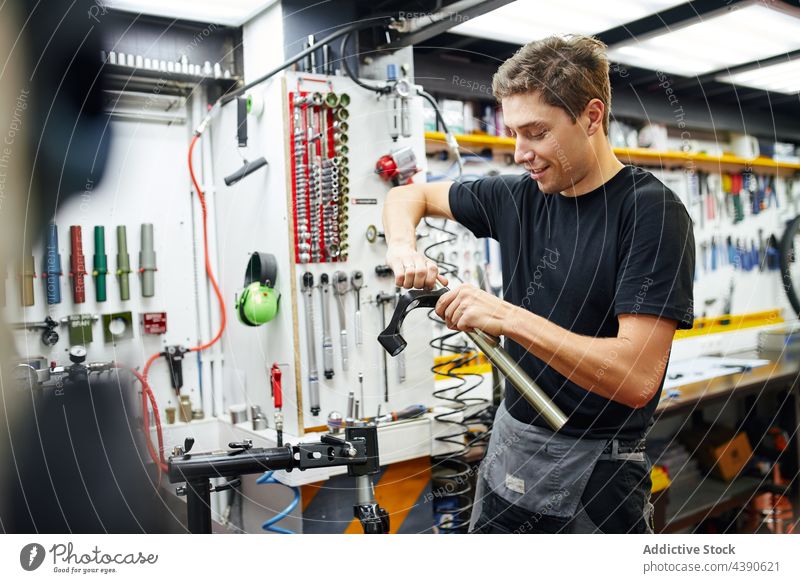 Lächelnder Mann, der in einer Garage eine Fahrradgabel repariert Mechaniker fixieren Reparatur Gabel Werkstatt Dienst männlich Werkzeug heiter Freude Inhalt