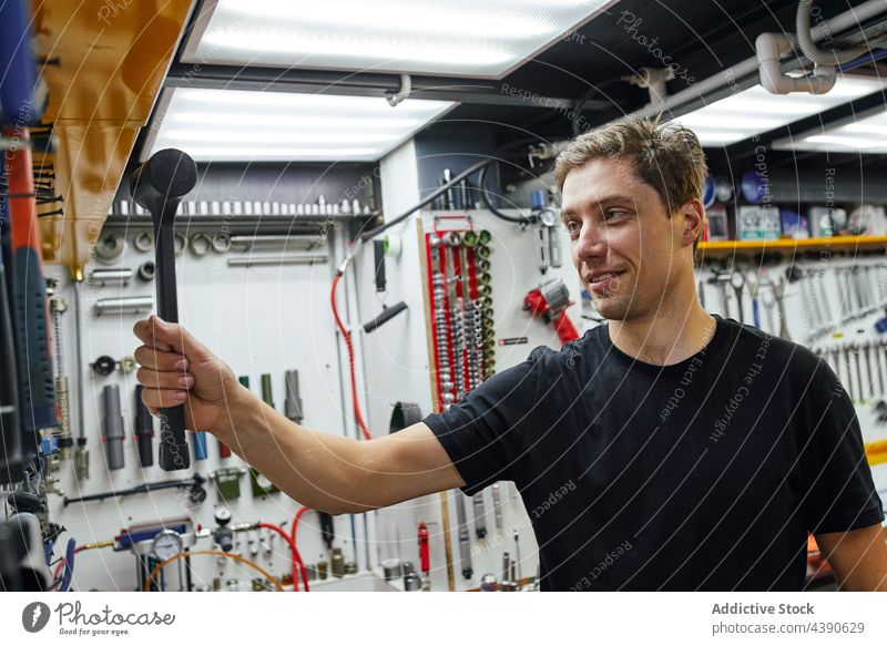 Männlicher Mechaniker mit Hammer in der Werkstatt Mann Arbeit Lächeln Wand Reparatur professionell Dienst männlich Erwachsener Job Beruf positiv Werkzeug